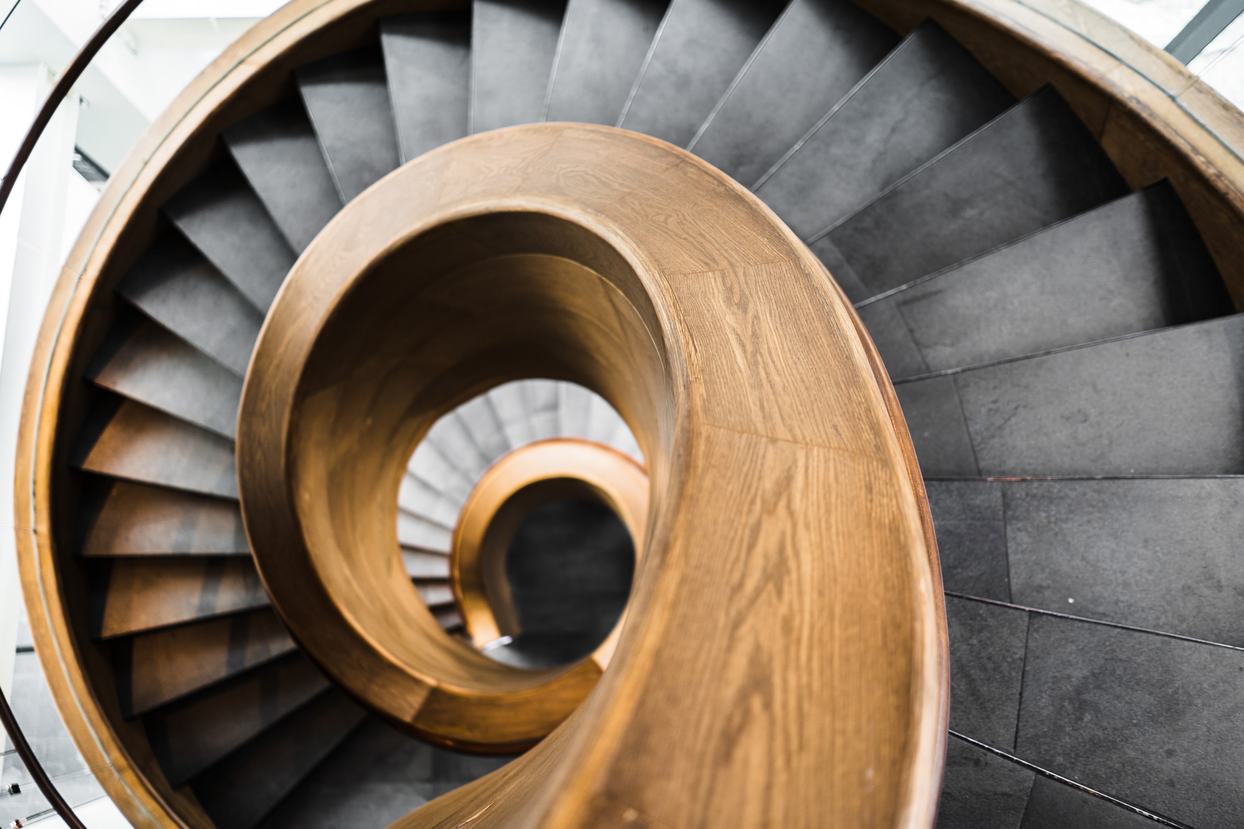 The lower treads of a spiral oak staircase curving away across stone.